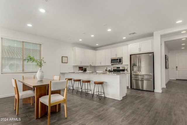 kitchen with light stone countertops, dark wood-type flooring, stainless steel appliances, kitchen peninsula, and white cabinets