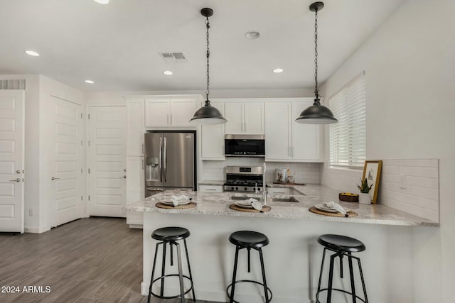 kitchen featuring kitchen peninsula, stainless steel appliances, wood-type flooring, decorative light fixtures, and white cabinetry