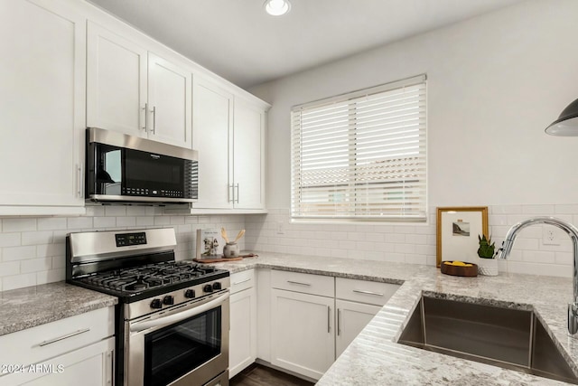 kitchen with light stone countertops, appliances with stainless steel finishes, tasteful backsplash, sink, and white cabinetry