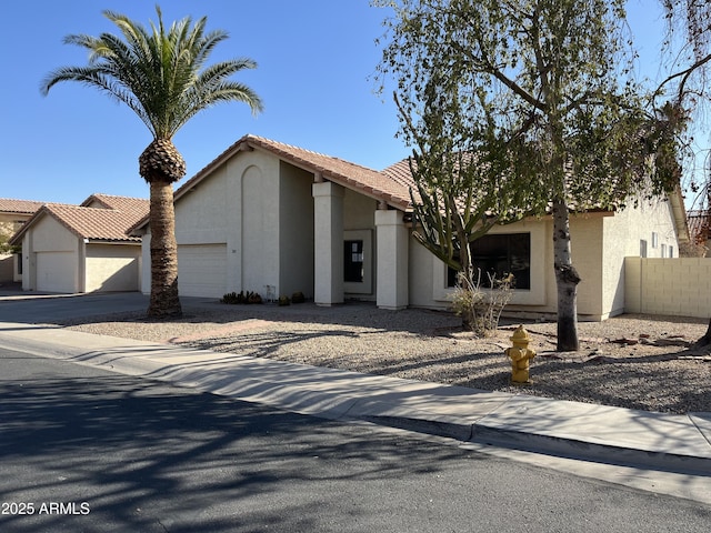 view of front of property with a garage, a tile roof, fence, and stucco siding