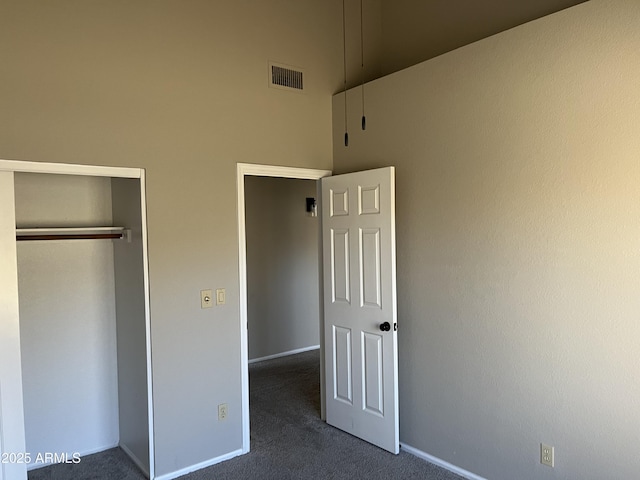 unfurnished bedroom with baseboards, visible vents, a high ceiling, dark carpet, and a closet