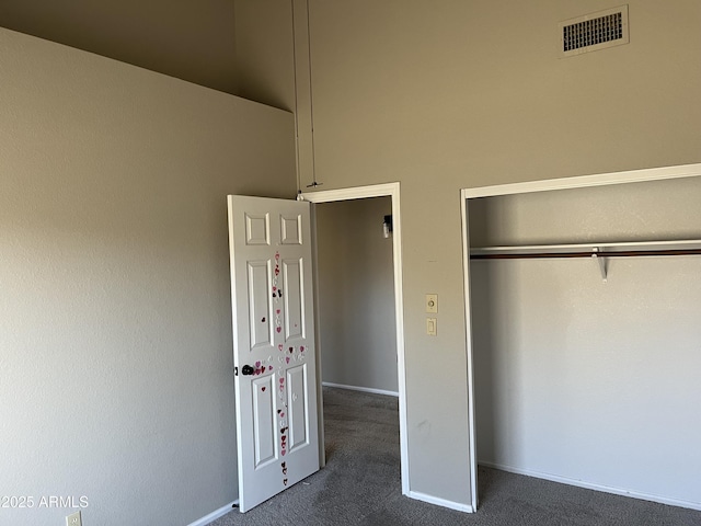 unfurnished bedroom with baseboards, visible vents, dark carpet, and a closet