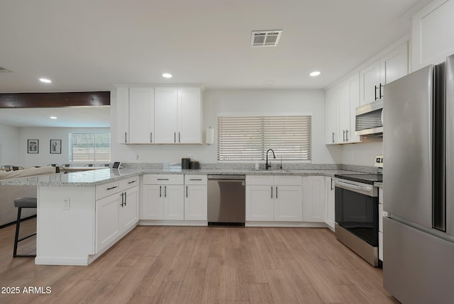 kitchen with a breakfast bar, white cabinetry, stainless steel appliances, kitchen peninsula, and light wood-type flooring