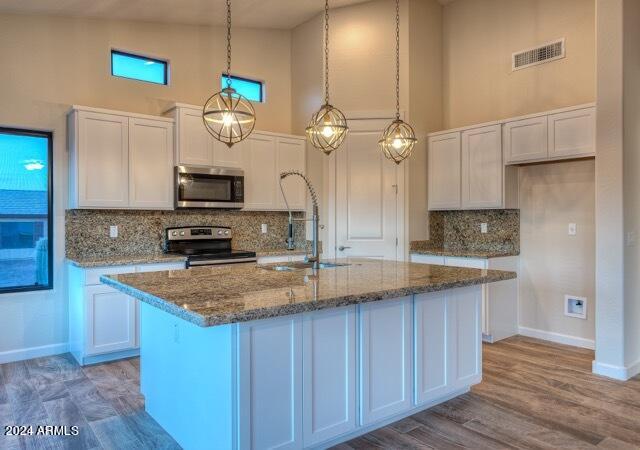 kitchen with white cabinetry, high vaulted ceiling, backsplash, an island with sink, and appliances with stainless steel finishes