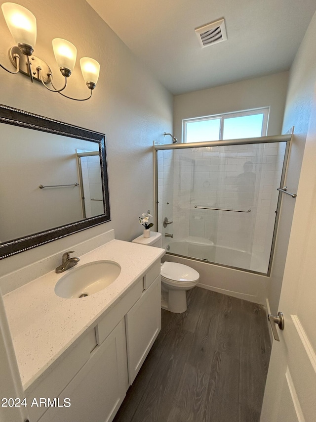 full bathroom featuring hardwood / wood-style flooring, vanity, toilet, and bath / shower combo with glass door