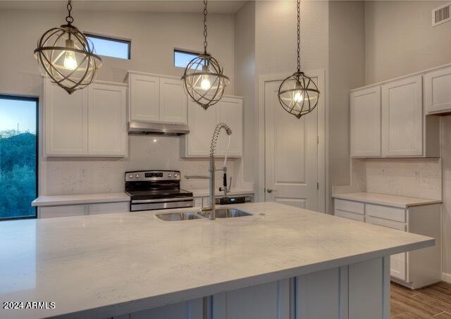 kitchen with stainless steel electric stove, white cabinets, high vaulted ceiling, and pendant lighting