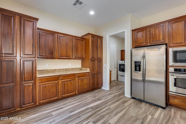 kitchen with stainless steel appliances, washer / clothes dryer, light stone countertops, and light wood-type flooring