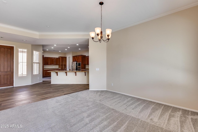 unfurnished living room featuring ornamental molding, a chandelier, and dark carpet