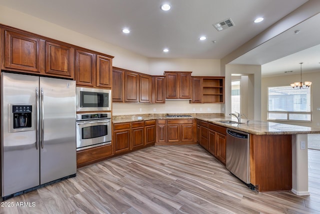 kitchen featuring sink, hanging light fixtures, stainless steel appliances, light hardwood / wood-style floors, and kitchen peninsula