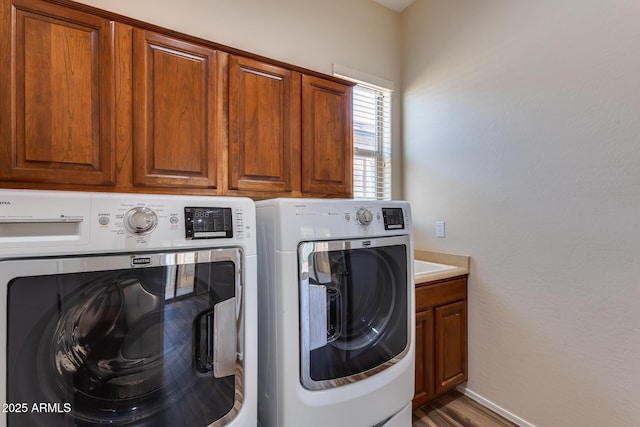 clothes washing area featuring cabinets, hardwood / wood-style floors, and washer and clothes dryer