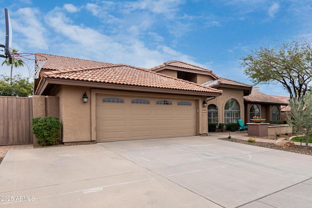 mediterranean / spanish house with fence, a tiled roof, concrete driveway, stucco siding, and an attached garage