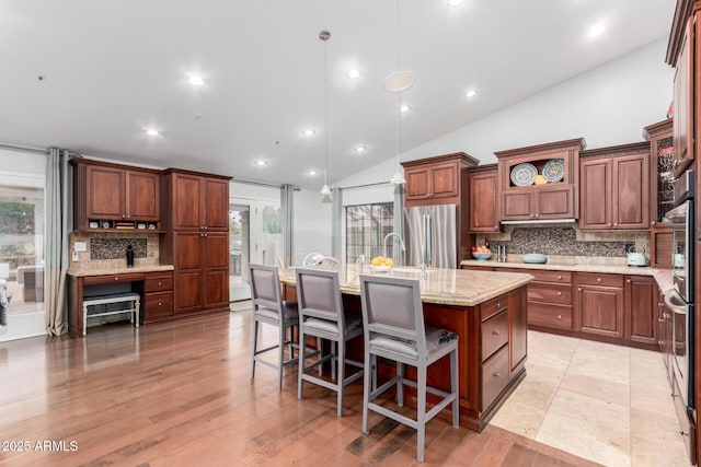 kitchen featuring light stone counters, open shelves, a kitchen island with sink, freestanding refrigerator, and tasteful backsplash