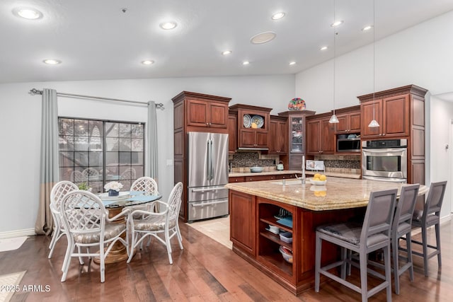 kitchen with a center island with sink, open shelves, a sink, backsplash, and appliances with stainless steel finishes