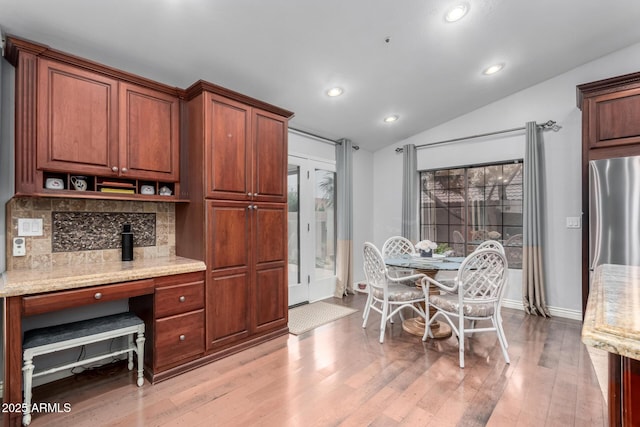 kitchen featuring light wood-style flooring, light stone counters, backsplash, freestanding refrigerator, and lofted ceiling