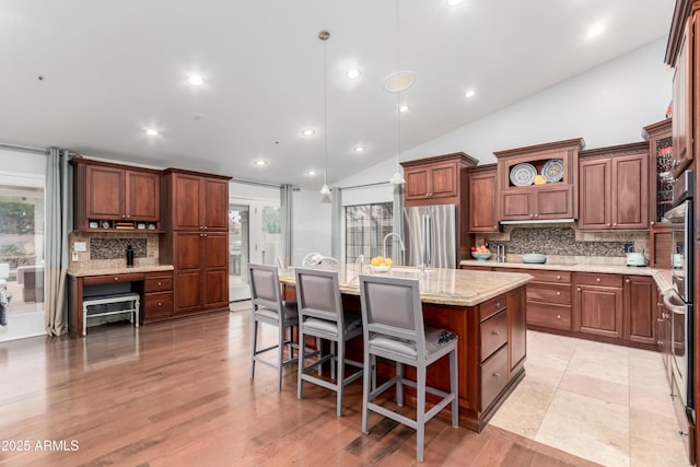 kitchen featuring backsplash, light stone countertops, a center island with sink, freestanding refrigerator, and open shelves