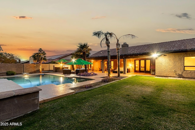 pool at dusk featuring a fenced in pool, french doors, a fenced backyard, a yard, and a patio