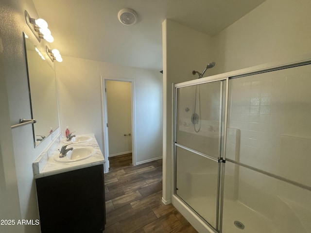 bathroom with a sink, double vanity, a shower stall, and wood finished floors