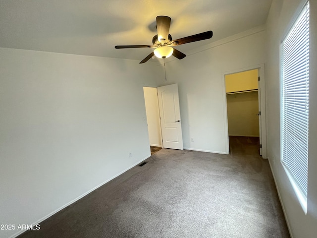 unfurnished bedroom with a ceiling fan, a closet, baseboards, dark colored carpet, and a spacious closet