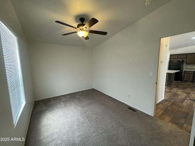 empty room with ceiling fan, dark colored carpet, baseboards, and visible vents