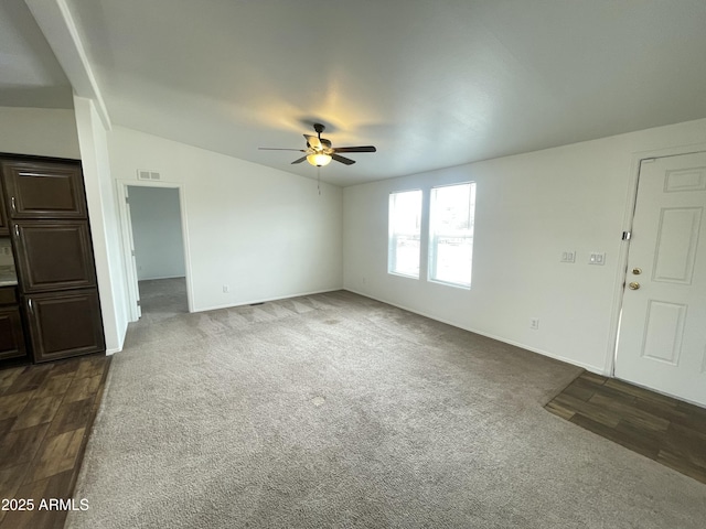 unfurnished living room featuring vaulted ceiling, ceiling fan, dark carpet, and dark wood finished floors