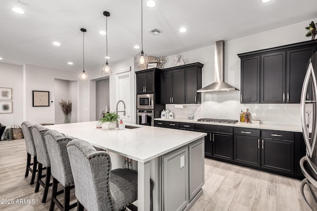 kitchen featuring pendant lighting, a spacious island, stainless steel appliances, a sink, and wall chimney range hood