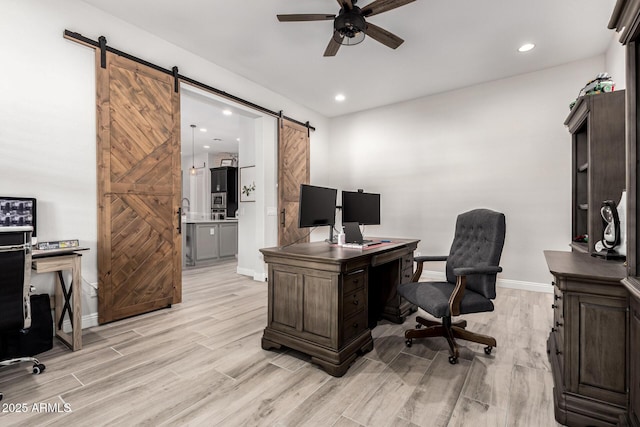 office space with ceiling fan, a barn door, light wood-type flooring, and baseboards