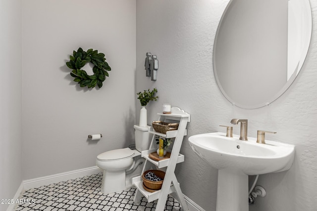 bathroom with a textured wall, a sink, toilet, and baseboards