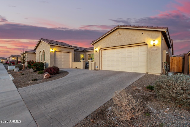 view of front of house featuring an attached garage, a tile roof, decorative driveway, and stucco siding