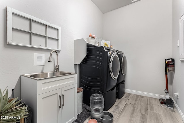 laundry room with cabinet space, light wood finished floors, baseboards, washing machine and dryer, and a sink