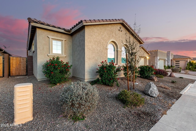 mediterranean / spanish-style house featuring fence, a tiled roof, and stucco siding