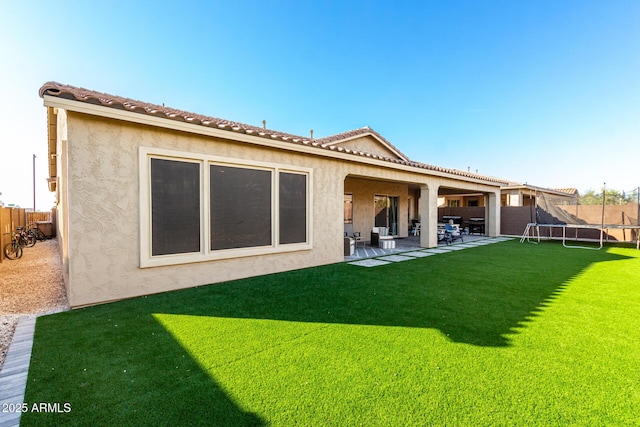 rear view of property featuring a trampoline, a tile roof, and stucco siding