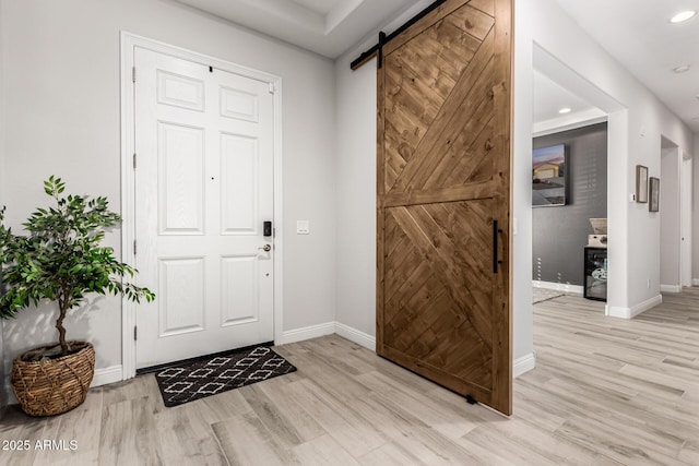 foyer entrance with light wood-type flooring, recessed lighting, baseboards, and a barn door