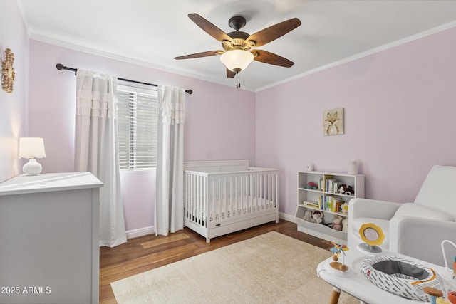 bedroom with ornamental molding, a nursery area, wood finished floors, ceiling fan, and baseboards