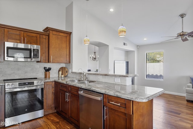 kitchen with appliances with stainless steel finishes, open floor plan, a peninsula, a sink, and decorative backsplash