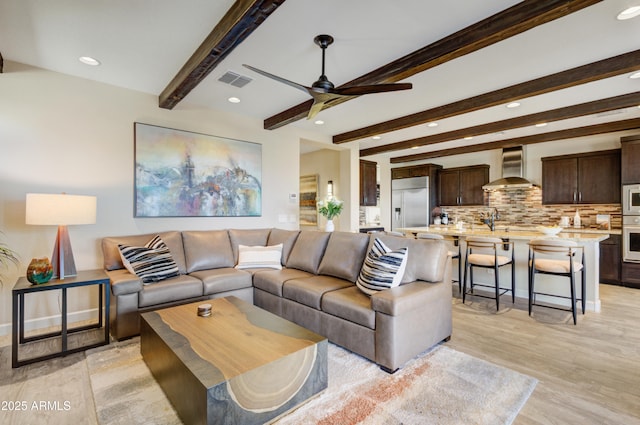 living room with ceiling fan, sink, light hardwood / wood-style flooring, and beam ceiling