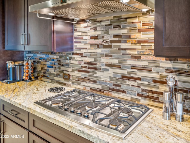 kitchen featuring stainless steel gas stovetop, light stone countertops, backsplash, and wall chimney range hood