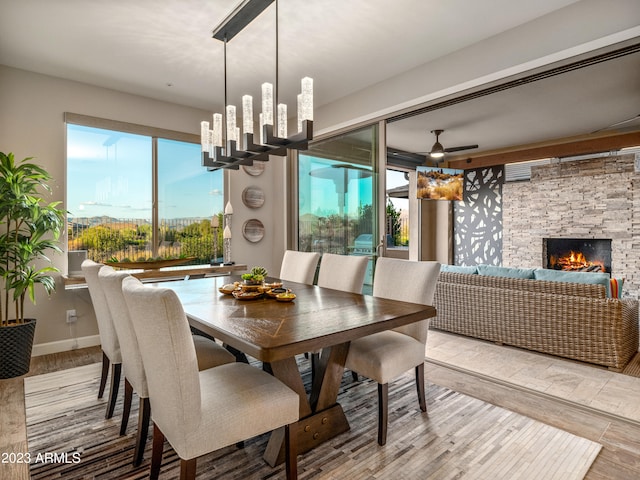 dining space with light wood-type flooring, ceiling fan, and a stone fireplace