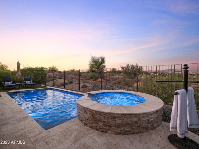 pool at dusk with a patio area and an in ground hot tub