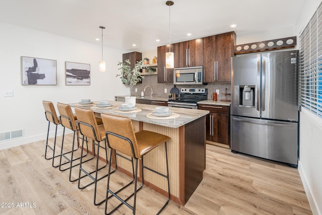 kitchen with a kitchen island, appliances with stainless steel finishes, decorative light fixtures, decorative backsplash, and light stone countertops