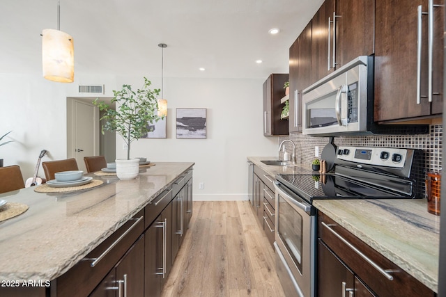 kitchen featuring dark brown cabinets, appliances with stainless steel finishes, hanging light fixtures, and backsplash