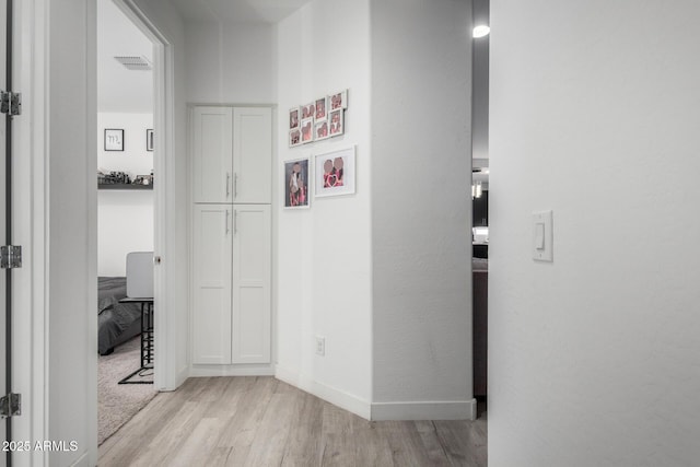 corridor with baseboards, visible vents, and light wood-style floors