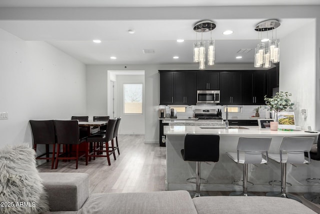 kitchen featuring appliances with stainless steel finishes, a sink, dark cabinetry, and a kitchen breakfast bar