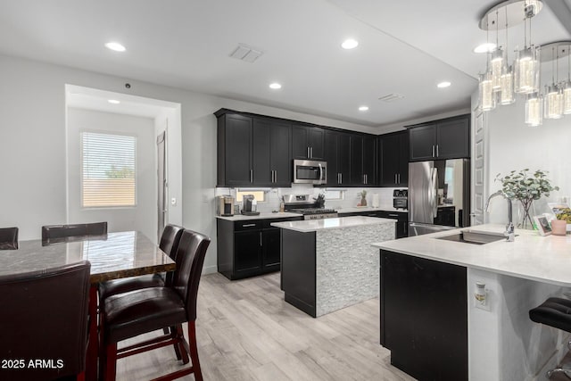 kitchen featuring light wood finished floors, a kitchen island, a breakfast bar, stainless steel appliances, and a sink