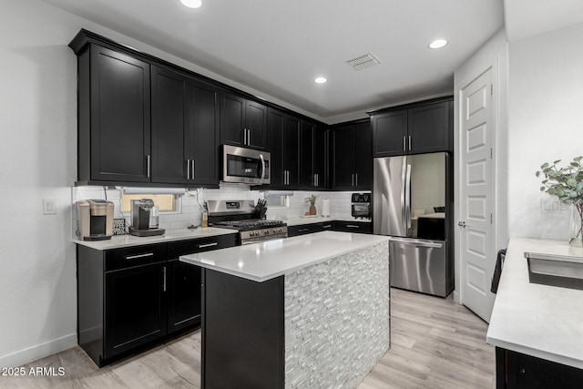 kitchen featuring decorative backsplash, stainless steel appliances, dark cabinetry, light countertops, and light wood-style floors