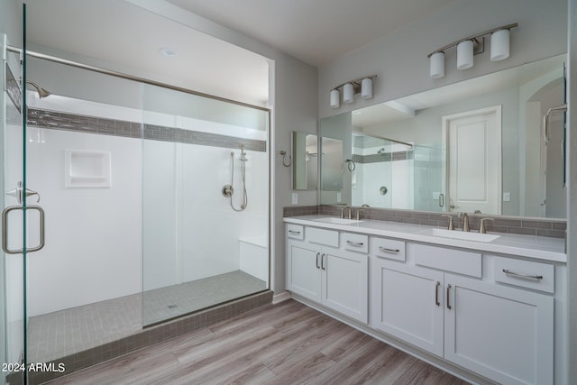 full bathroom with double vanity, a sink, a shower stall, and wood finished floors