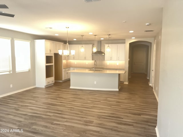 kitchen featuring white cabinetry, decorative light fixtures, wall chimney range hood, dark hardwood / wood-style flooring, and an island with sink