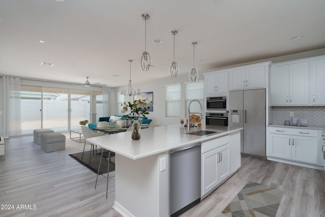 kitchen with light wood-style flooring, appliances with stainless steel finishes, white cabinetry, a sink, and backsplash
