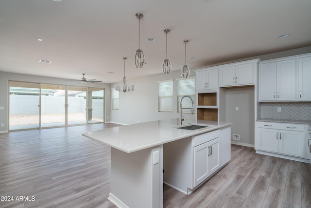 kitchen with backsplash, a sink, an island with sink, light wood-style floors, and ceiling fan