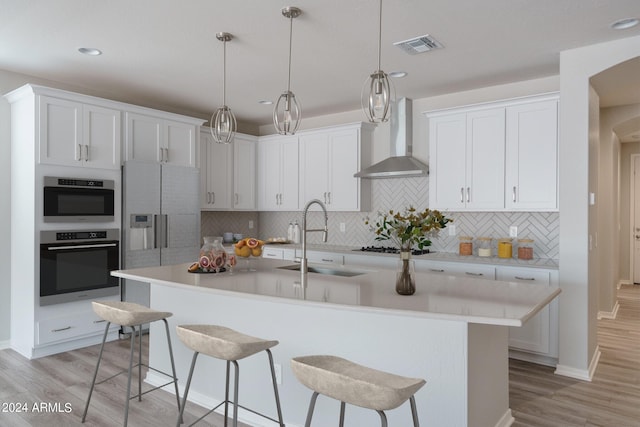 kitchen with wall chimney range hood, a breakfast bar area, light countertops, and a sink