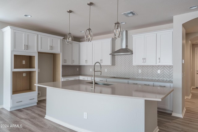 kitchen with wall chimney range hood, a center island with sink, wood finished floors, and a sink